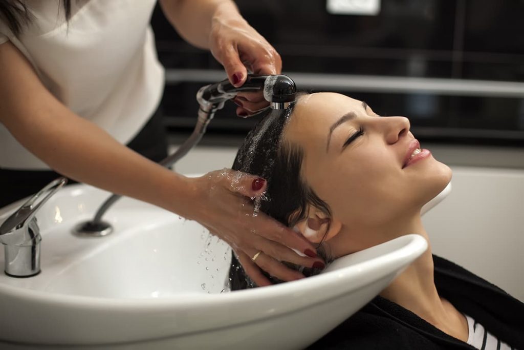 A cosmetologist washing a client's hair